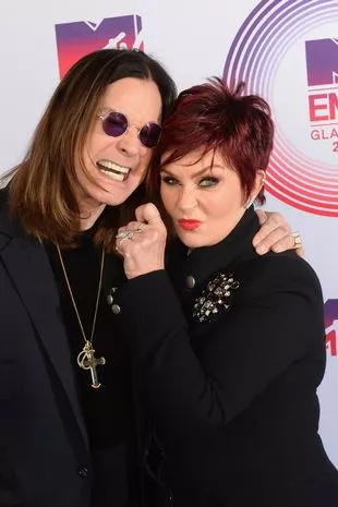 A red carpet picture of a snuggling Ozzy and Sharon Osbourne, both wearing black