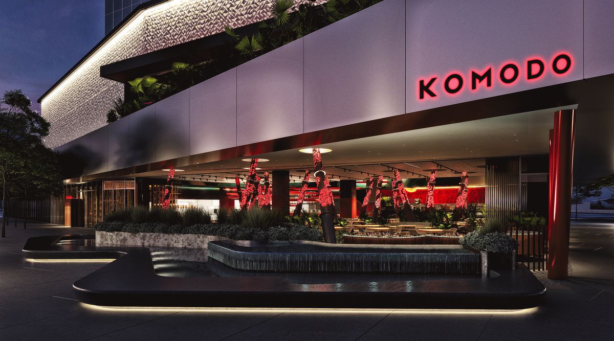 An exterior of a modern restaurant with red columns, a water feature, and white ceilings/exterior. A sign read “Komodo” in red letters.