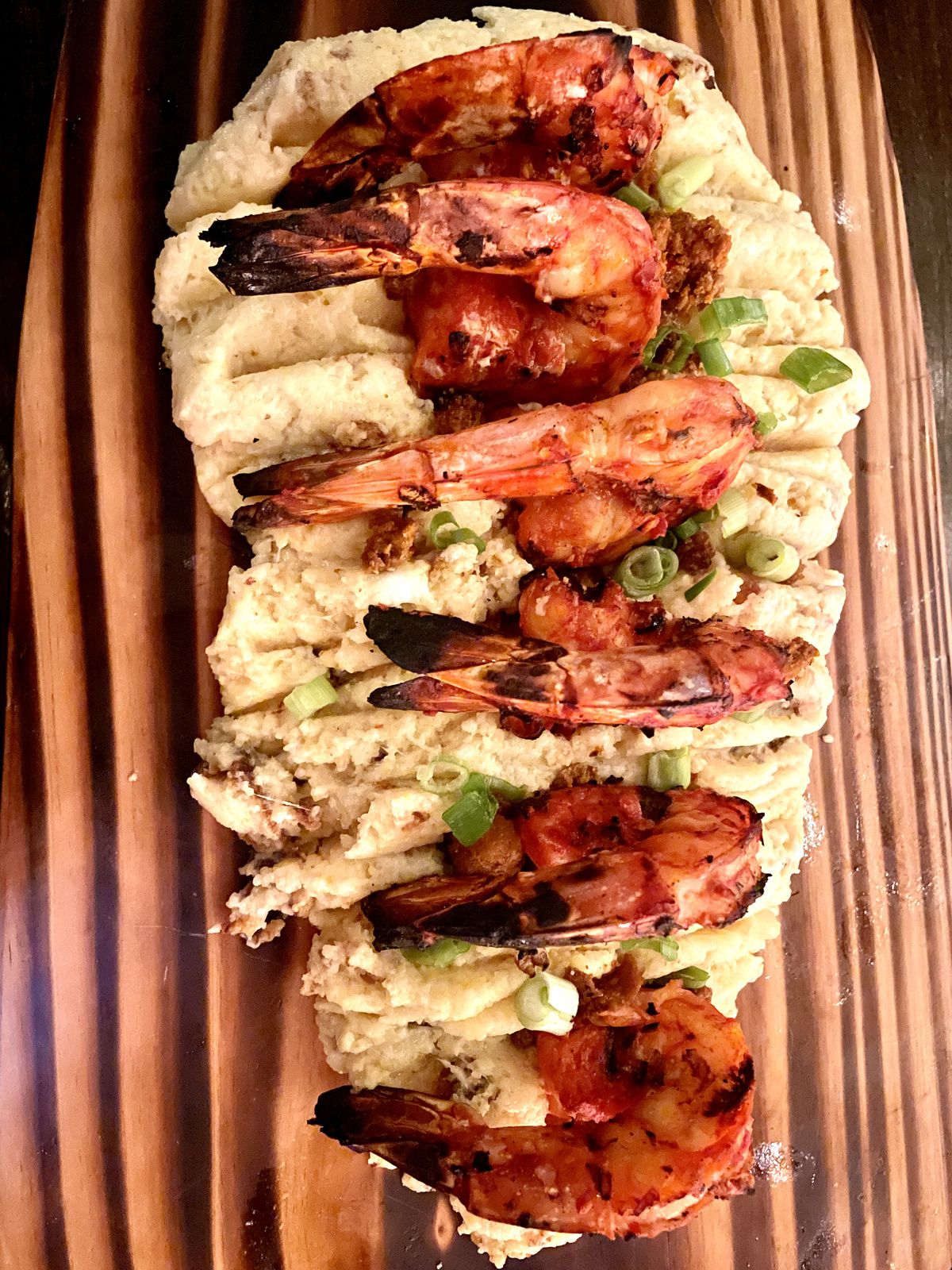 A board covered in mashed potatoes with grilled shrimp stuck into them. 