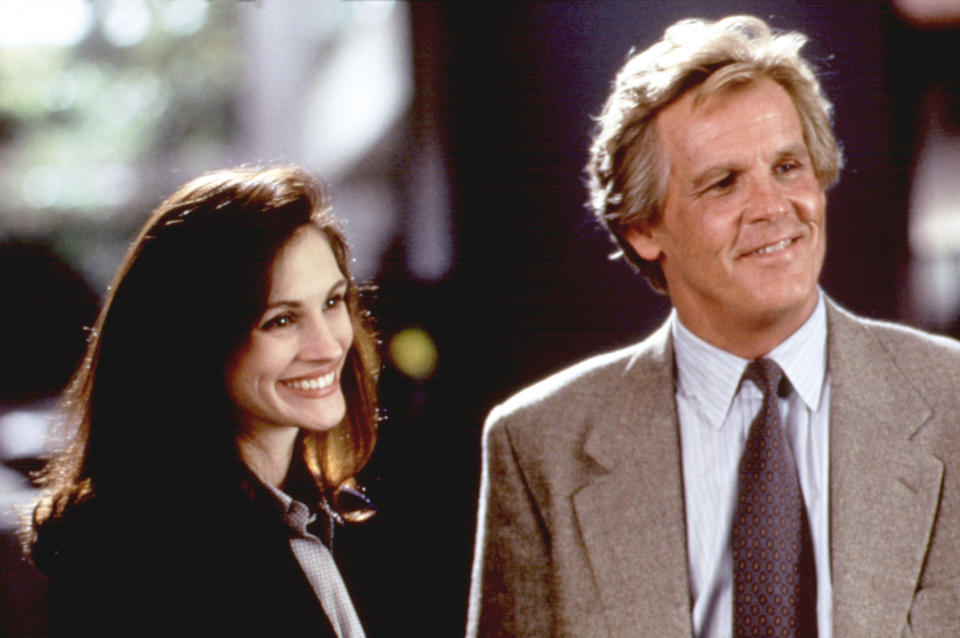 Julia Roberts smiles next to Nick Nolte. She wears a business suit while he dons a light blazer and tie