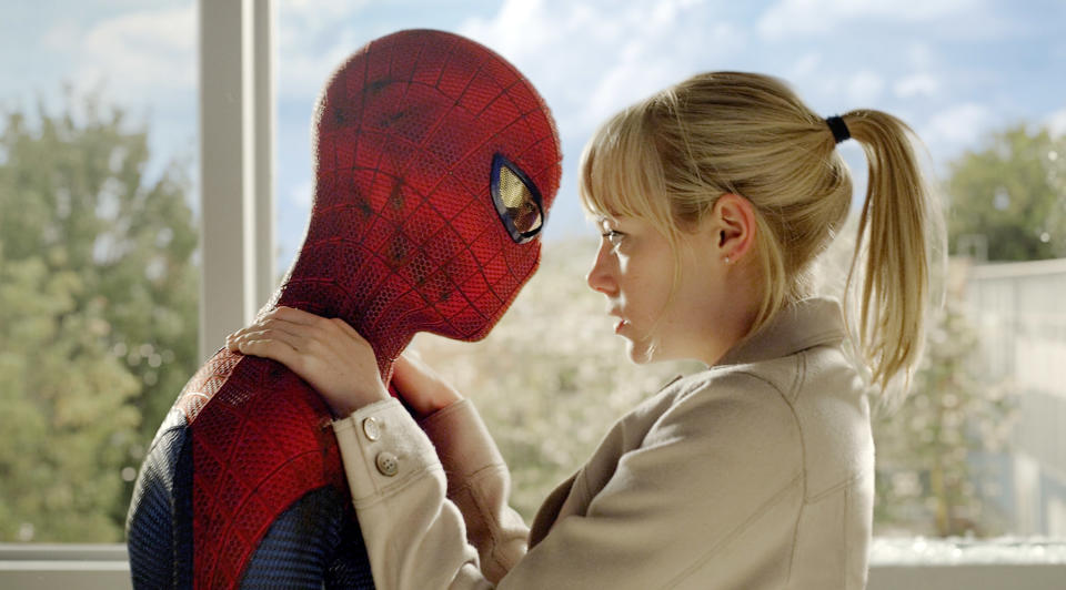 Spider-Man, in his iconic suit, shares an emotional moment with Gwen Stacy, who holds his face in her hands, against a backdrop of trees and a cloudy sky